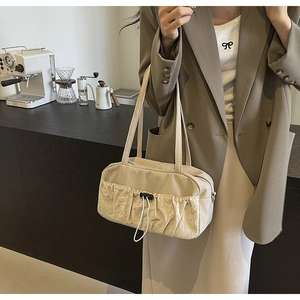 Detailed close-up of cream pleated shoulder bag with drawstring detail in a cafe setting