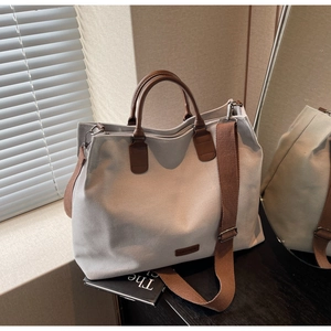 Detail of grey nylon tote bag with brown leather handles on dark wood tabletop