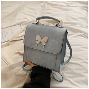 Détail d'un mini sac à dos bleu clair avec boucle papillon dorée sur lin blanc