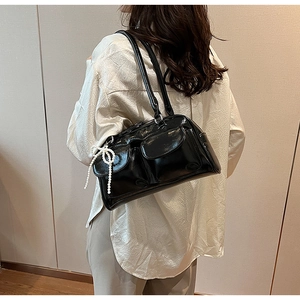 Detail of black glossy underarm bag with double front pockets and pearl bow charm