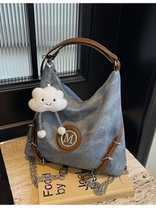 Blue washed denim shoulder bag with leather trim, metal M logo, and chain strap