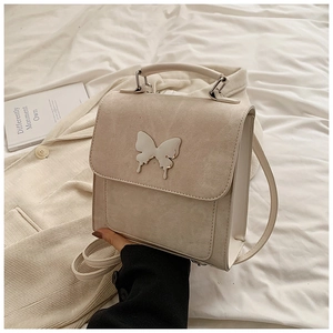 Détail du sac à main carré en cuir crème orné d'un papillon métallique argenté élégant