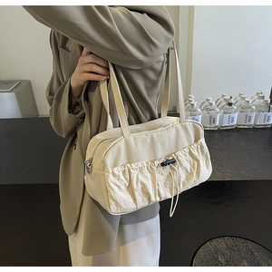Detail of a creamy white pleated shoulder bag with drawstring pocket and smooth zip closure