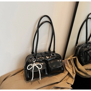 Detail of black glossy Boston bag with front pockets and pearl bow accessory