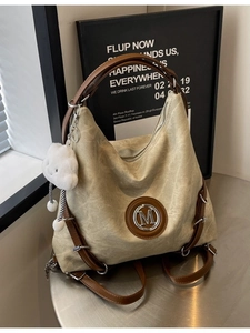 Large oatmeal canvas backpack with leather straps and metallic M logo on a round table