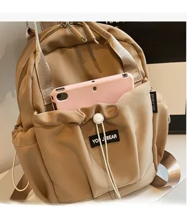 Detail of khaki nylon backpack featuring a drawstring pocket and front brand patch