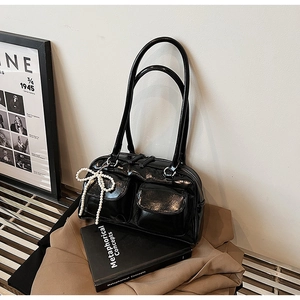 Close-up of black glossy Boston bag with flap pockets and a pearl bow charm
