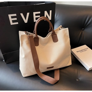 Close-up of cream canvas tote bag with brown handles on a minimalist leather sofa