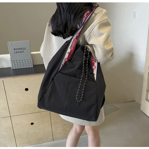 Vista de detalle de un bolso tote de nailon negro con correa deportiva tricolor ancha