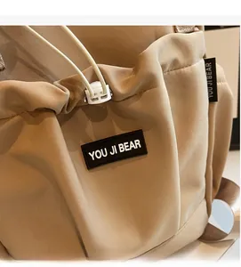 Detail of khaki nylon backpack featuring a brand patch and white adjustable drawstring closure