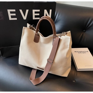 Detailed close-up of a beige canvas tote bag with brown leather handles on a black sofa