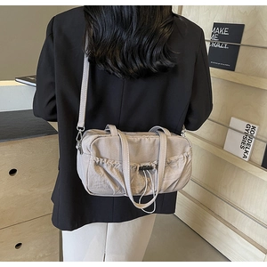 Detail of light grey pleated shoulder bag with adjustable straps on a wooden shelf