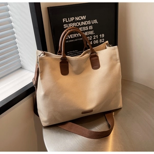 Close-up of cream canvas tote bag with brown leather handles and wide shoulder strap