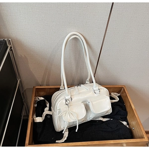 Close-up of cream Boston bag with double pockets and pearl bow charm on a wooden tray