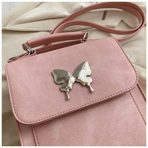 Gros plan du sac bandoulière rose texturé avec ornement papillon en métal argenté