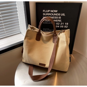 Detail of beige nylon tote bag featuring brown leather handles and brand logo patch