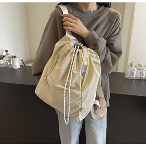 Detalle de la mochila de nailon beige con correa morada y cordón trenzado de cierre