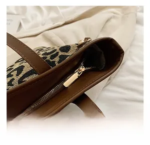 Close-up of golden zipper hardware and brown leather trim on leopard print tote bag