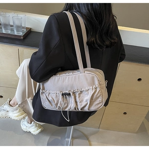 Lifestyle shot of light gray pleated shoulder bag with drawstrings on model in home setting