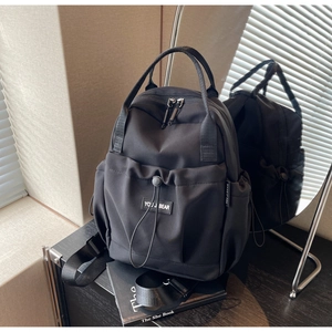 Close-up of black nylon backpack with drawstring pocket and adjustable straps on display