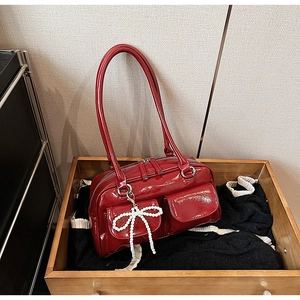 Detailed close-up of glossy red Boston bag featuring front pockets and pearl bow charm