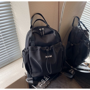 Black nylon travel backpack with double handles, drawstring front pocket, and adjustable straps