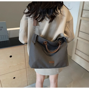 Detail of dark grey nylon tote bag with brown leather handles and a wide shoulder strap