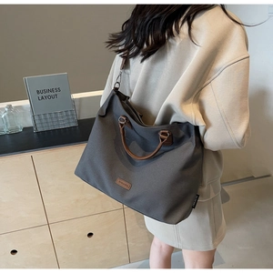 Detail of charcoal nylon tote bag with brown leather handles worn by a model in office