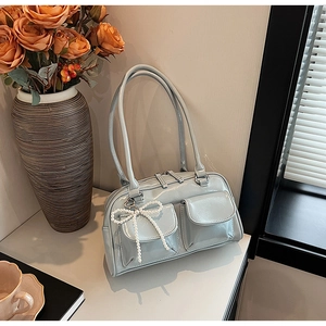 Detail of light blue glossy Boston bag featuring front flap pockets and pearl bow charm