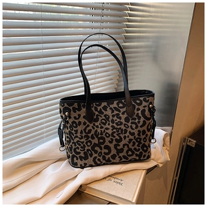 Close-up of leopard print canvas tote bag featuring black leather handles and gold hardware