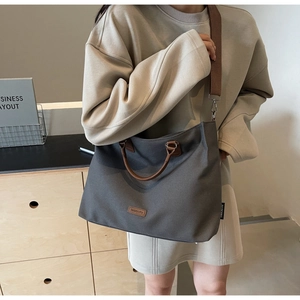 Model wearing a dark gray nylon tote bag with leather handles and wide shoulder strap
