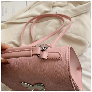 Détail du sac bandoulière rose avec ornement papillon argenté et texture fine de cuir