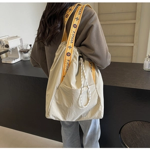 Detalle de un bolso tote grande de lona beige con correa de hombro ancha amarilla estampada