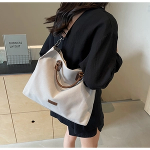 Close-up of large canvas tote bag with brown leather handles and adjustable shoulder strap