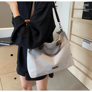 Detail view of a grey canvas tote bag with adjustable brown leather straps and brand logo
