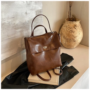 Detail of a brown leather backpack with silver turn-lock and unique stitched textures