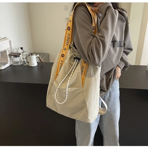 Detalle del bolso tote beige con correas amarillas decoradas con motivos vibrantes