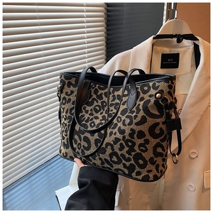 Detail of leopard print tote bag with black leather handles and golden metal buckle