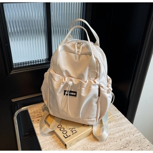 Detail of cream nylon backpack featuring dual top handles and drawstring front pocket