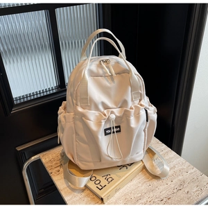 Detail of light beige nylon backpack featuring reinforced dual handles and drawstrings