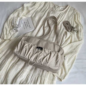 Detailed top view of beige pleated tote bag with adjustable strap on white fabric