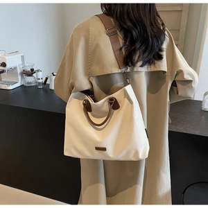 Beige nylon tote bag with brown leather handles worn by a model in a café scene