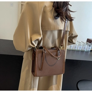 Detail einer dunkelbraunen Lederhandtasche mit weißen Nähten auf einem khakifarbenen Trenchcoat