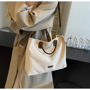 Detail of minimalist beige nylon tote bag with brown leather handles worn with a beige trench coat