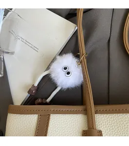 Dettaglio del ciondolo a pompon in peluche bianca su borsa tote in pelle