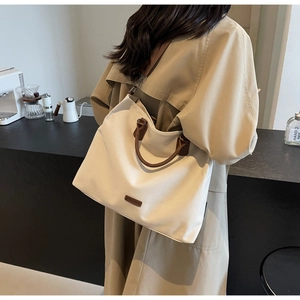 Detail of a beige nylon tote bag with brown leather handles in a cozy cafe setting