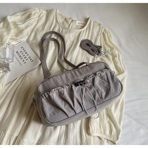 Detail of pleated grey shoulder bag with drawstring pocket on a soft fabric background