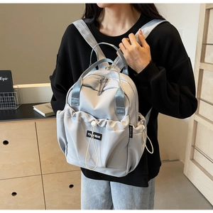 Detail of grey nylon backpack featuring front drawstring pocket and brand woven label