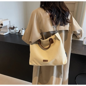 Nylon tote bag with brown leather handles worn by a model in a cozy cafe setting