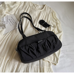 Detail of black pleated shoulder bag with adjustable strap on cream textured background